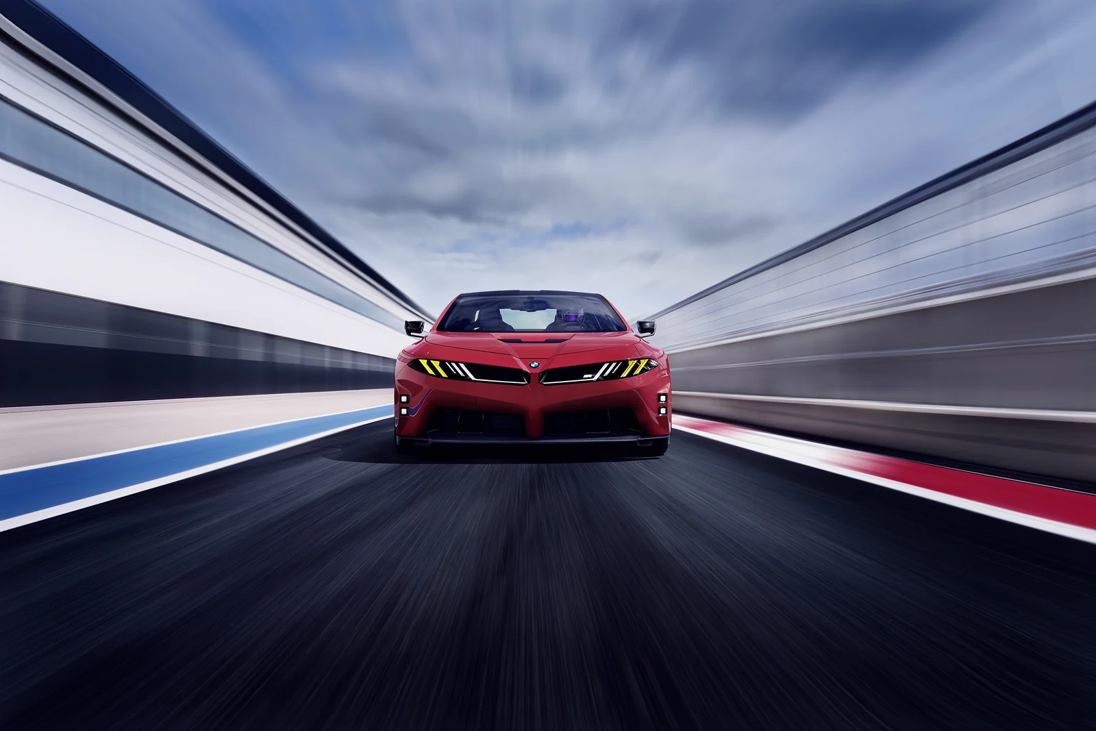 Röd BMW M Concept Neue Klasse rakt framifrån på en racerbana, med gula ljus i fronten.