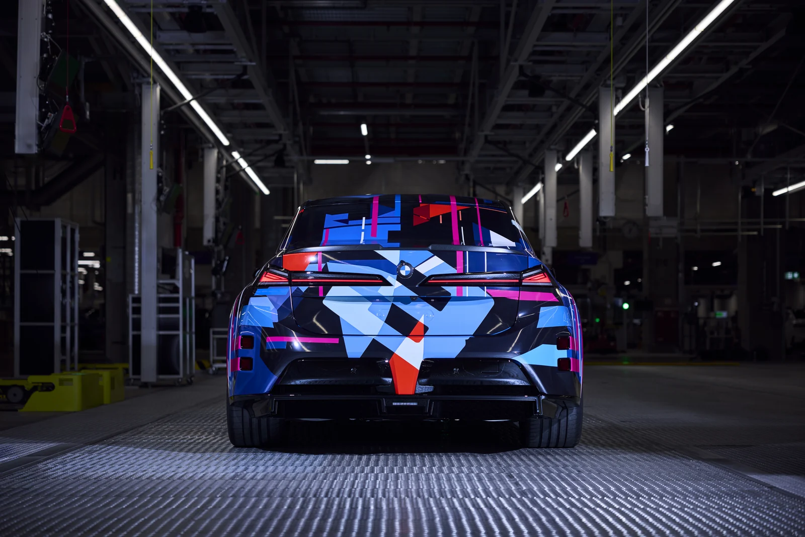 Den kamouflerade elektriska BMW M3:an rakt bakifrån i fabrikshallen i München.